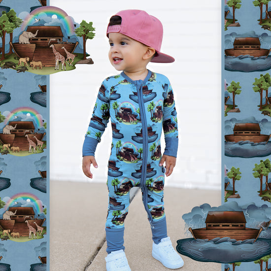 Child wearing a blue onesie with Noah's Ark design, standing in front of a patterned background.